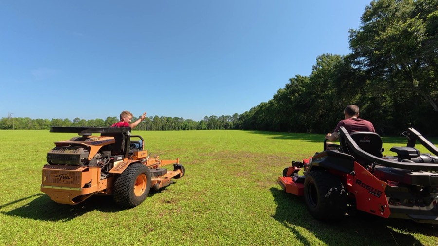 Two of the crew mowing a big open field on the Scag and the Bad Boy zero-turns under a blue sky