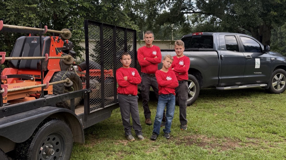 All four of the crew in matching red Three Brothers shirts, arms crossed, between the loaded equipment trailer and the Tundra
