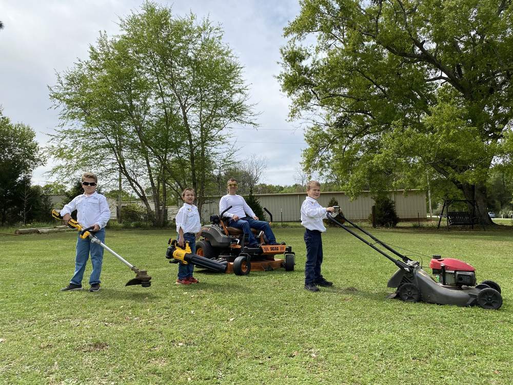 The original crew in the early days — three young boys with trimmer, blower, and mower, and Dad on the zero-turn